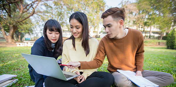 Group of students collaborating, sitting outside and working at a laptop