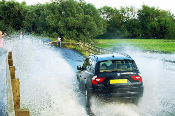 photo of a car driving over a flooded bridge