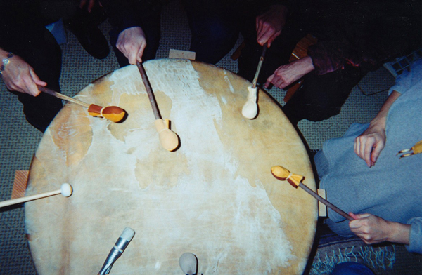 photo by Carptrash (CC BY-SA 4.0) photo of several people sitting around a large drum with many different drumsticks